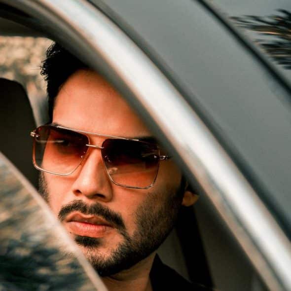 A man wearing sunglasses looking out a car window.