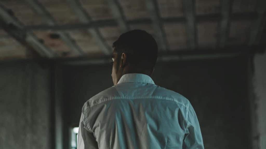 A man seen from behind standing alone in a dimly lit room.