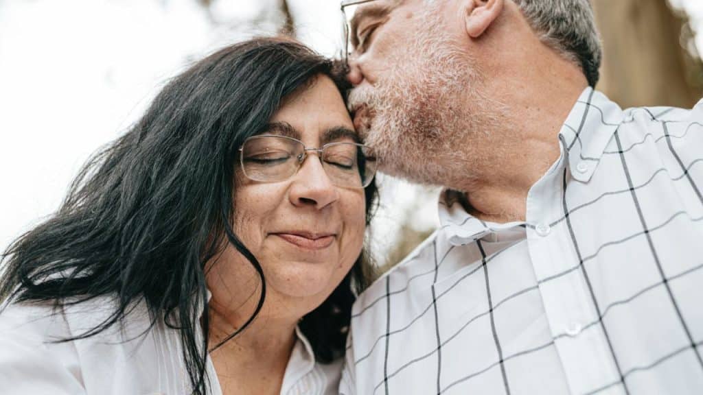 Close-up of a smiling woman with eyes closed, receiving a forehead kiss from a man.