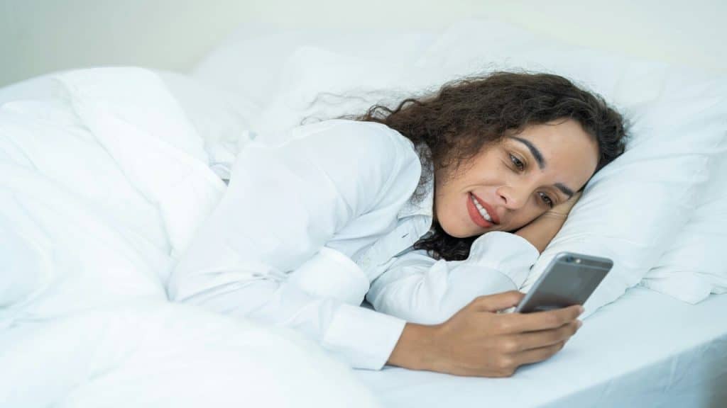 A woman smiling while texting in bed