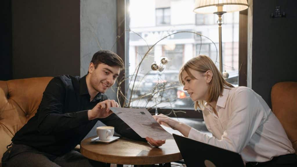 A man and a woman discussing a document at a café table.