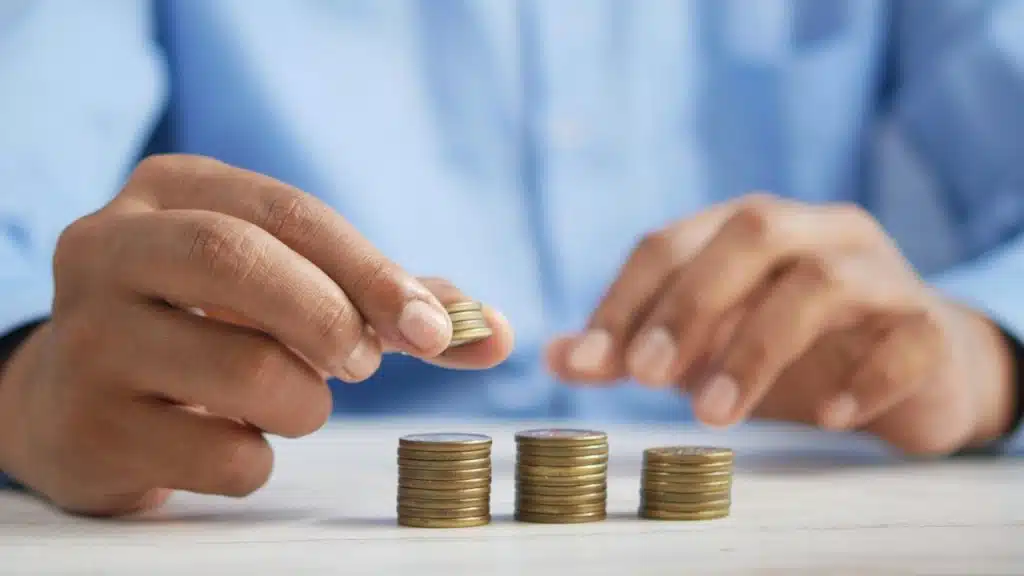 A close-up of a person's hands stacking a small pile of golden coins on a table.