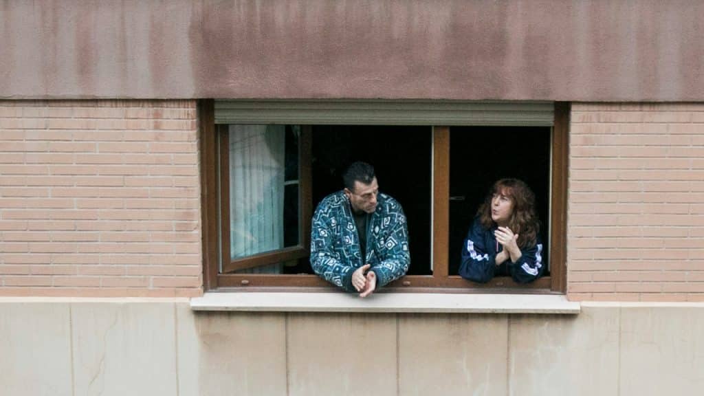 A man and a woman standing at the window of their house.