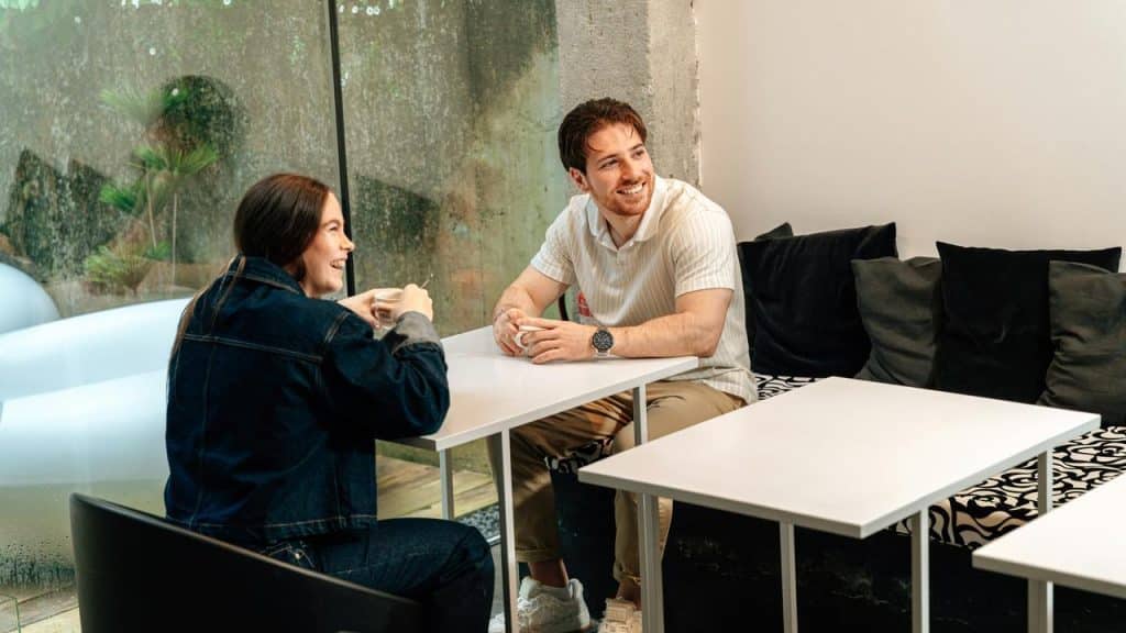 A man and woman sitting at a café table smiling and talking.