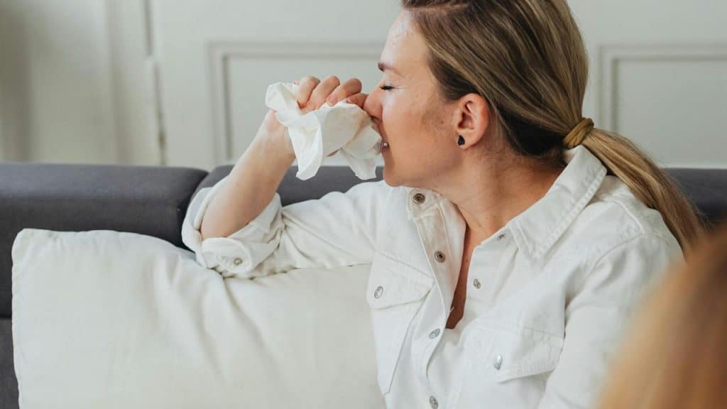 A woman sitting on a couch holding a tissue to her nose.