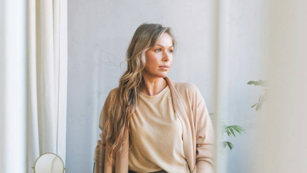 Woman with long wavy hair in a beige cardigan looking thoughtfully to the side.
