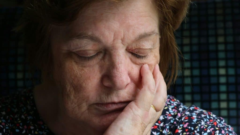 Close-up of an older woman with her eyes closed, hand resting on her face.