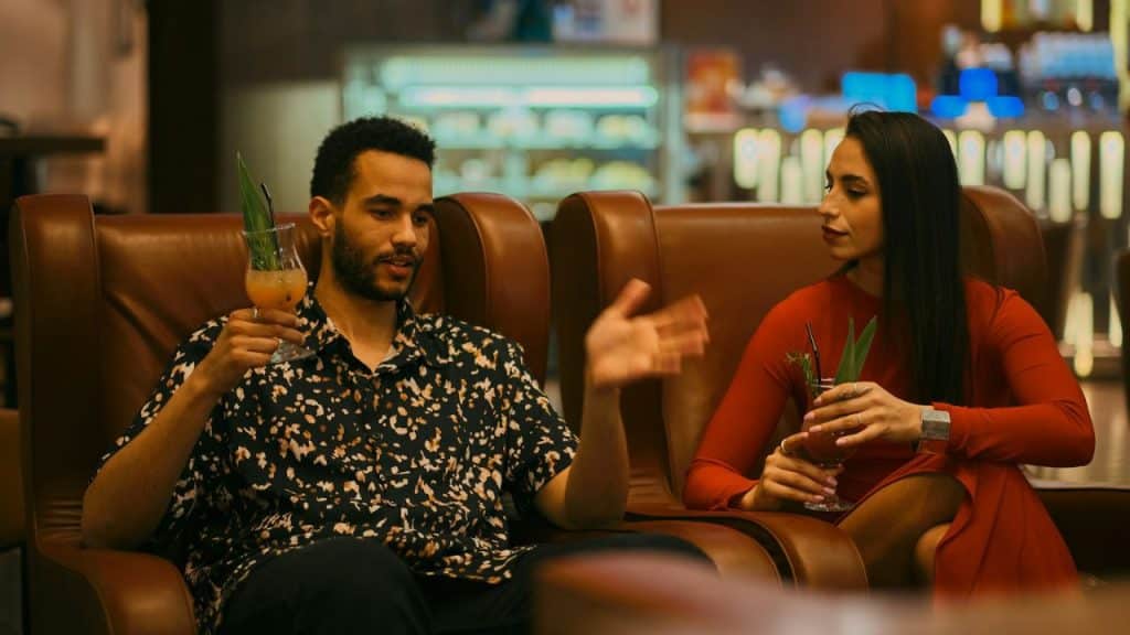 Man in patterned shirt talking and gesturing to a woman in a red dress.
