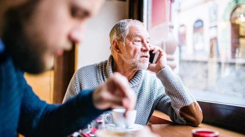 An older man talking on the phone while sitting in a café.