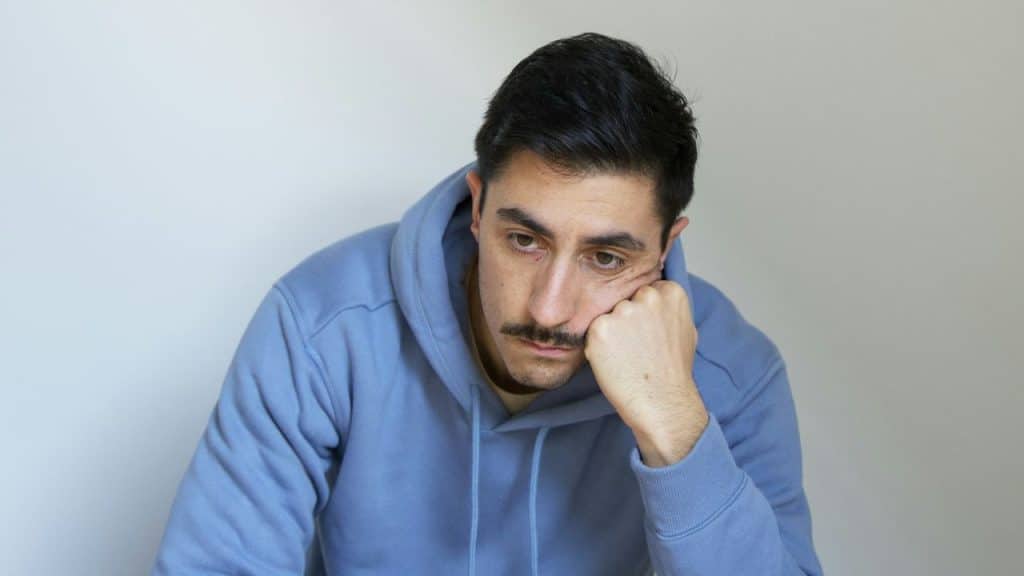 A man with a mustache looks downward while resting his face on his hand.