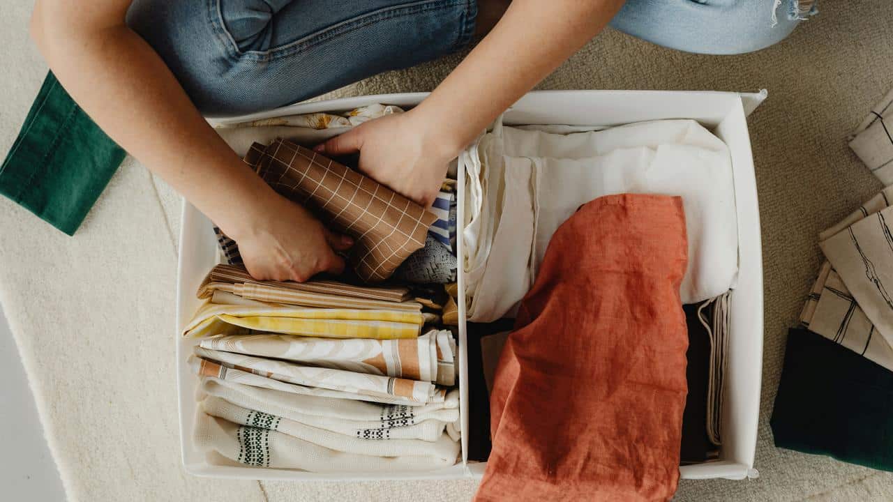 A person organizing folded fabrics in a storage box.