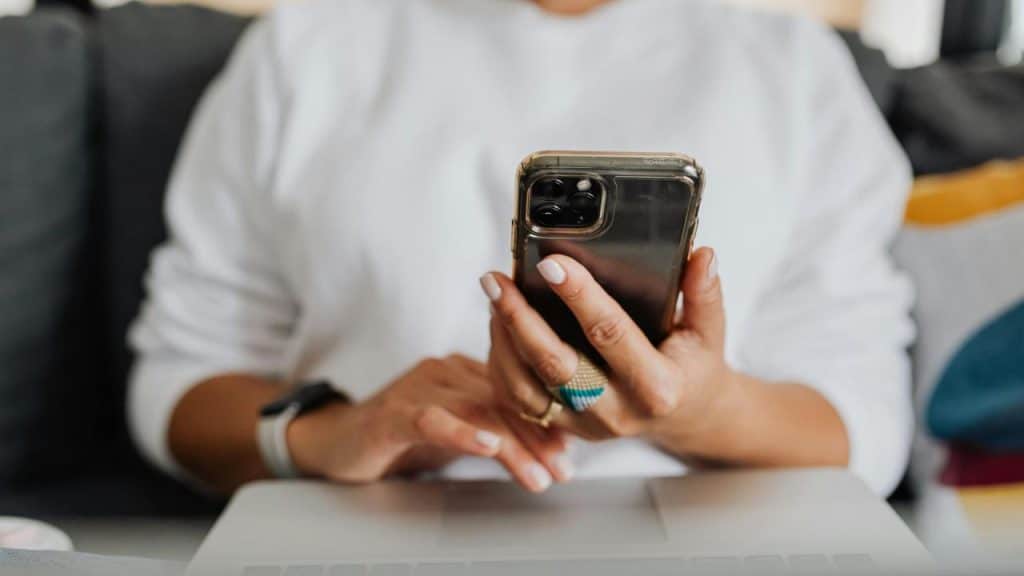 A person using a smartphone while sitting in front of a laptop.