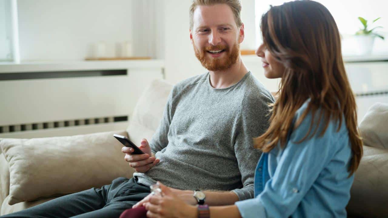 A man and woman sitting on a couch smiling and talking.
