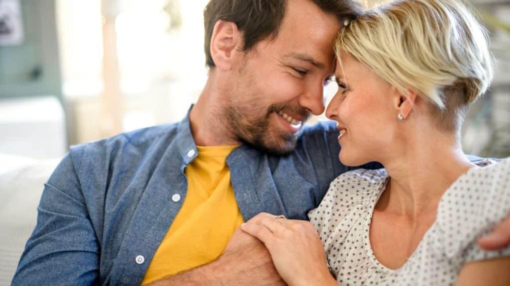 A smiling man and woman look at each other with their foreheads touching.