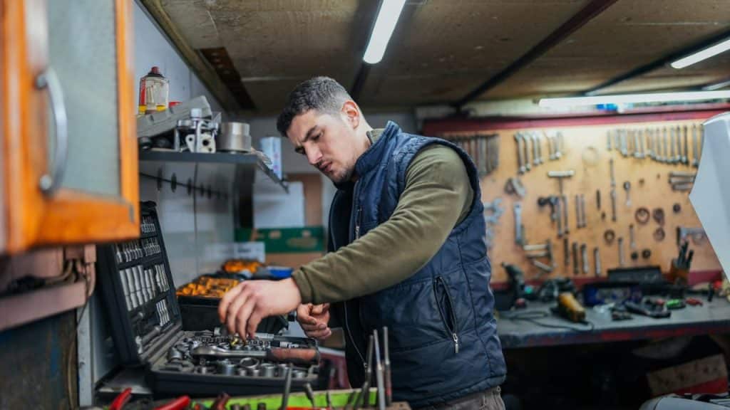 A man in a blue vest works with a toolset in a cluttered garage or workshop.