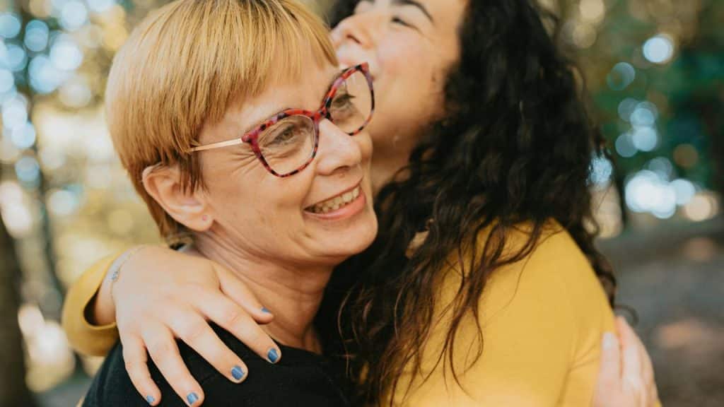 An older woman happily hugging a younger woman outdoors.