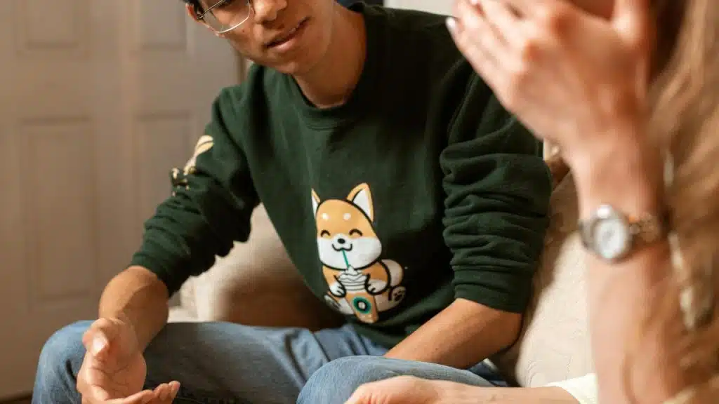 A person talking with another person while sitting on a couch indoors.