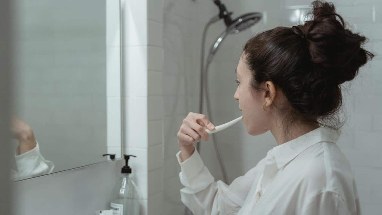 A woman brushes her teeth in front of a bathroom mirror.