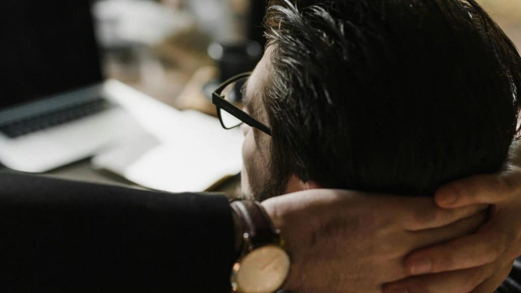 A man leaning back in a chair with his hands behind his head at a desk.