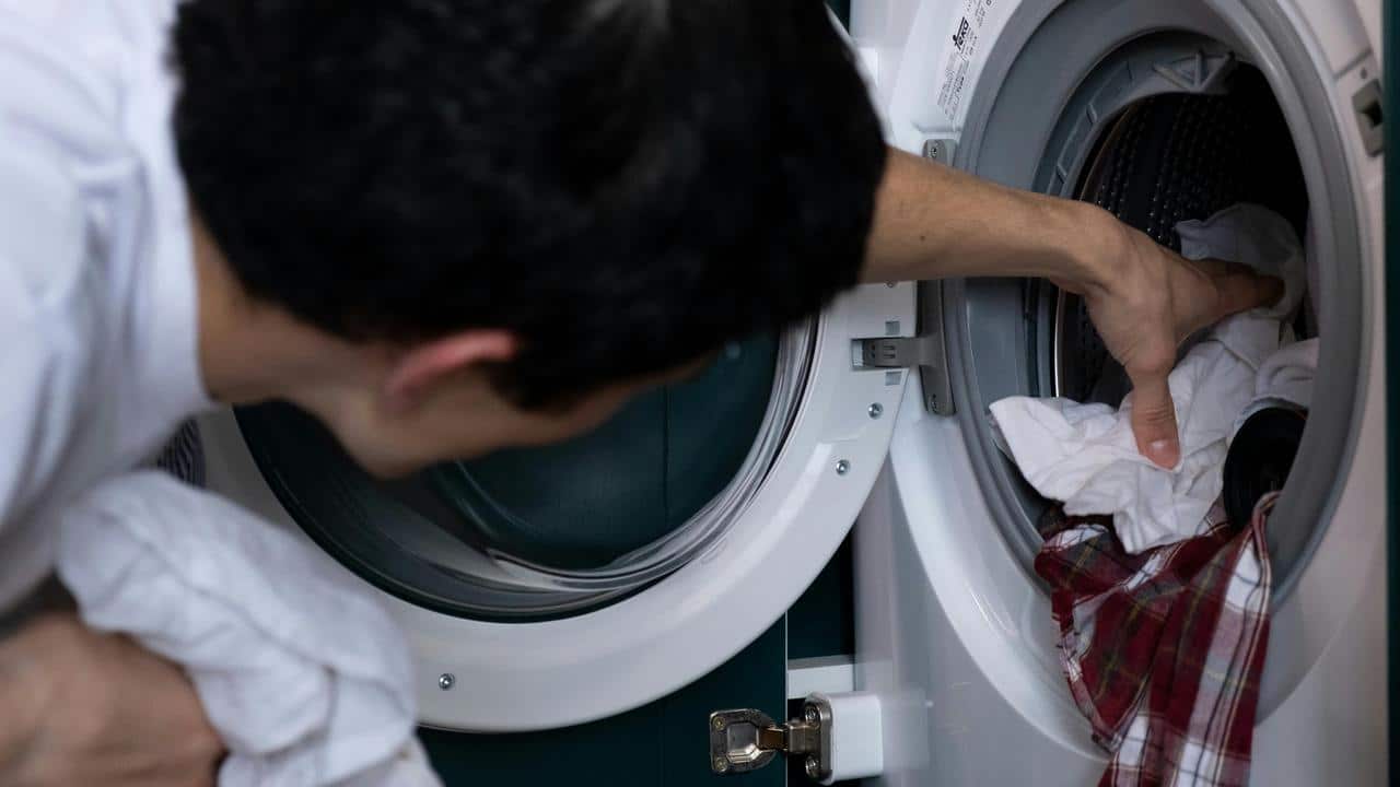 A person loading clothes into a washing machine.