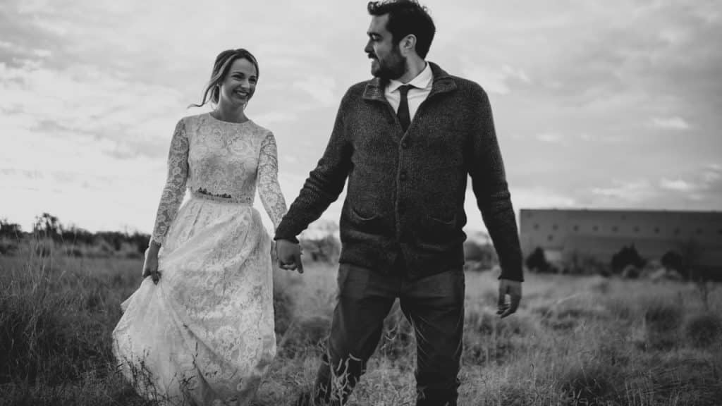 A man and a woman walking through a field holding hands.
