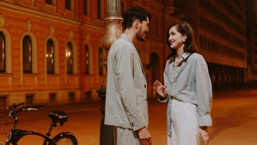 A couple talking at night near a lamppost and a bicycle.