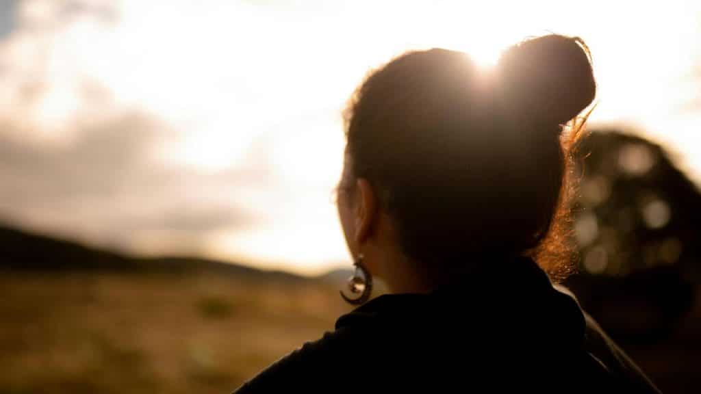 A woman facing a bright sunset with her hair in a bun.