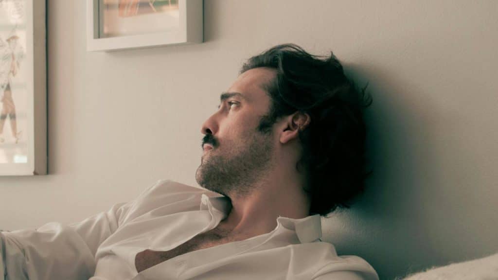 A man reclining against a wall looks off to the side.