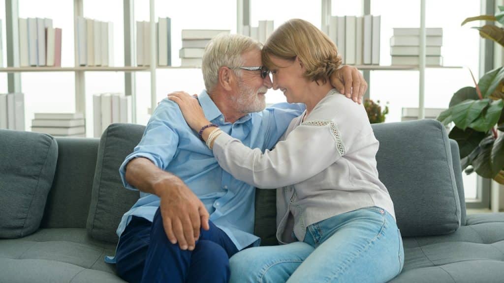 A happy senior couple embracing each other while they are sitting in a living room.