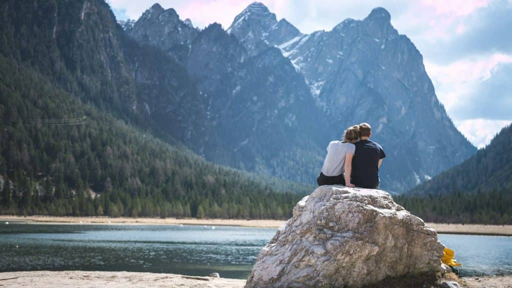 A couple sits on a rock looking out over a lake.