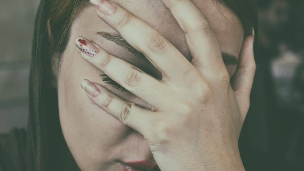A woman looking upset and hiding her face with her hand.