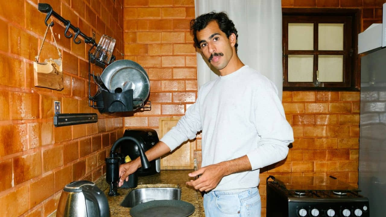 Man with a mustache standing in a rustic brick kitchen next to a sink.