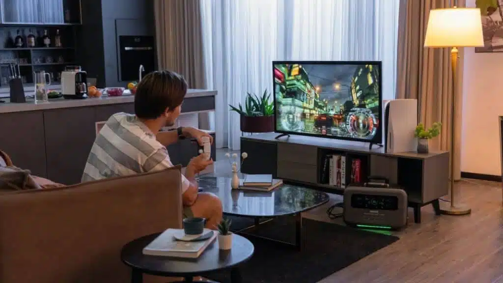 A young man sits on a couch playing a video game on a large TV in a modern living room.