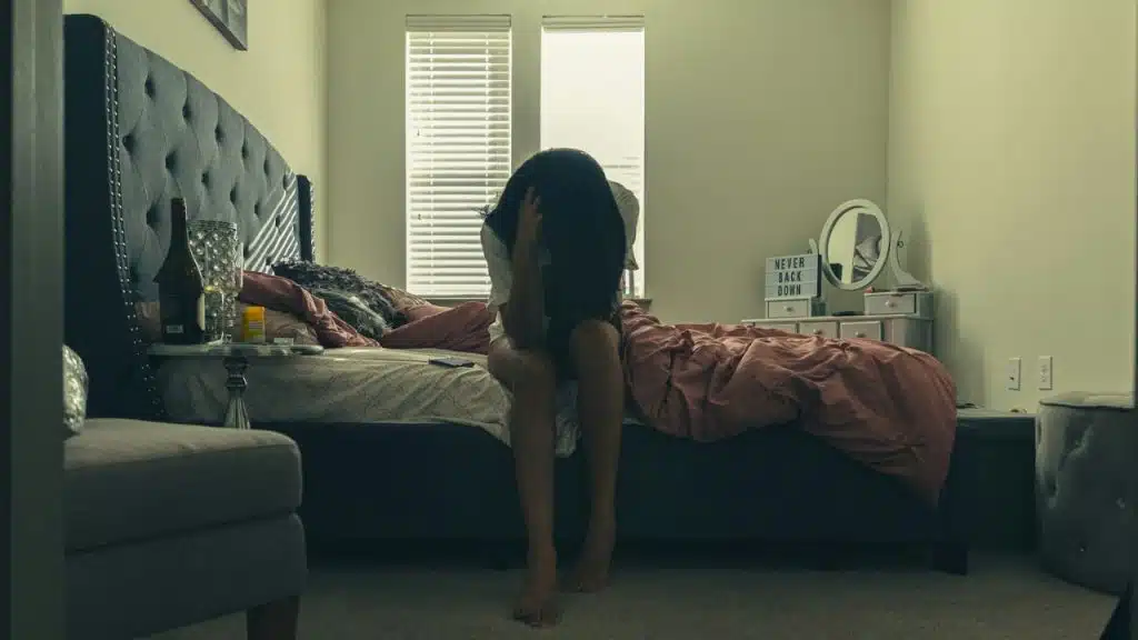 A person sitting on the edge of a bed with their face hidden by their hair.