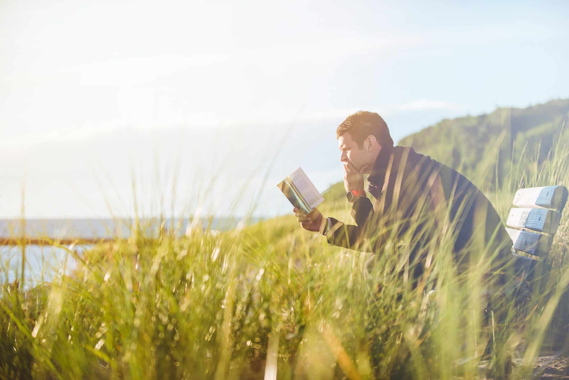 A man reading a book near the lake.