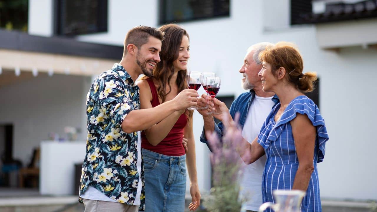 Two couples, one younger and one older, making a toast with glasses of red wine outdoors.