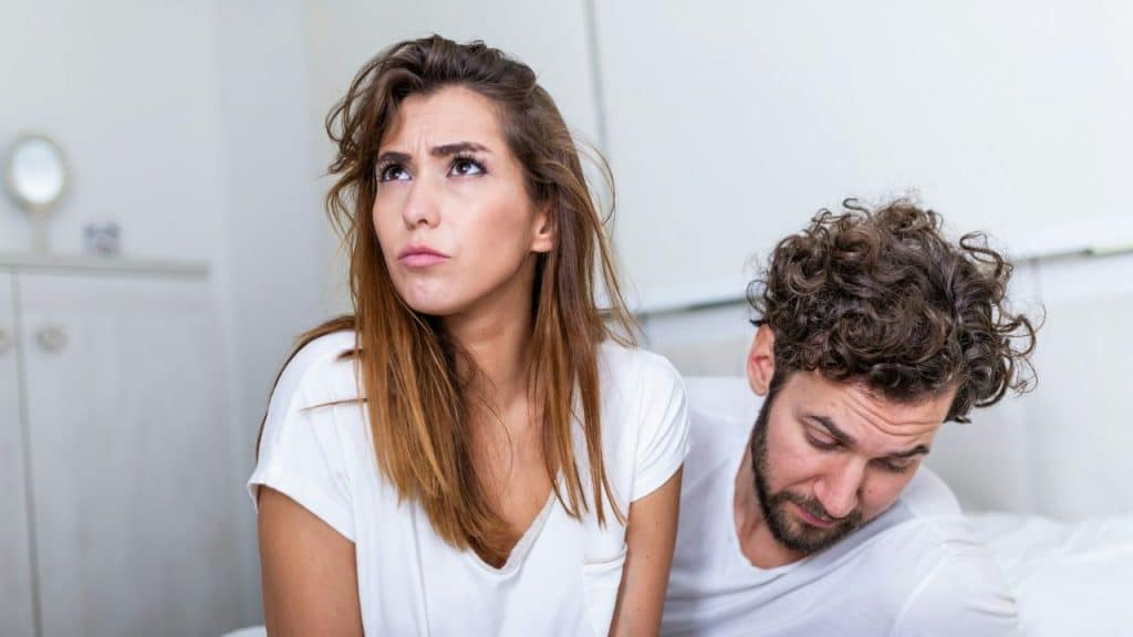 Woman looking upward with a distressed expression, man looks down in the background.