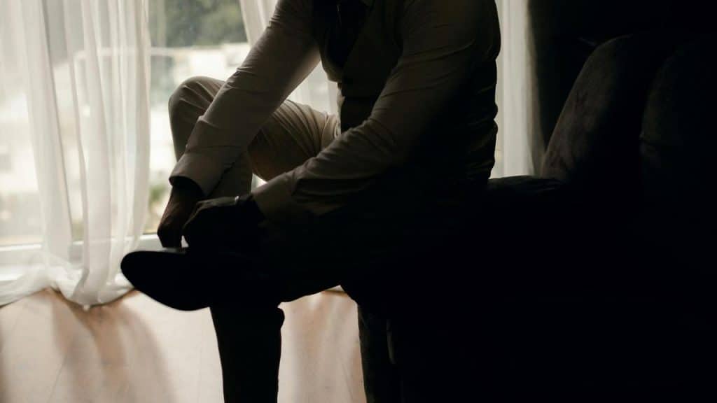 A silhouette of a man adjusting his shoe near a window.