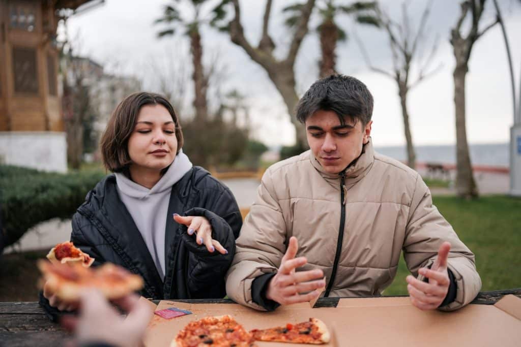 A couple sitting at a table, eating pizza.