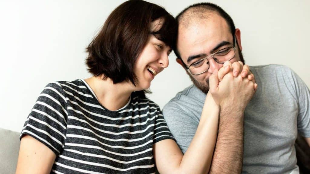 Happy couple holding hands, man looking down and kissing the woman's hands.