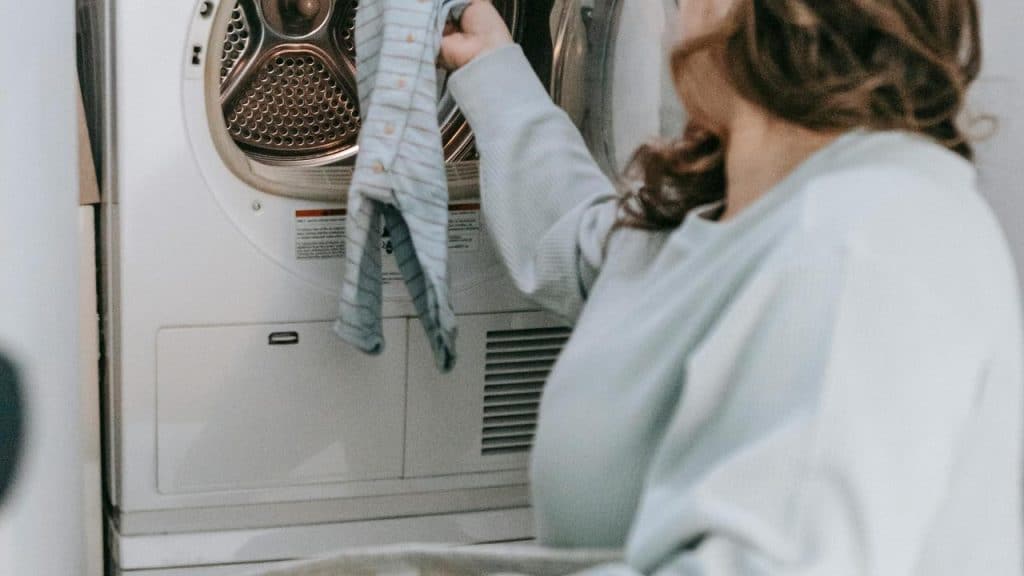 A woman placing a baby onesie into a dryer.