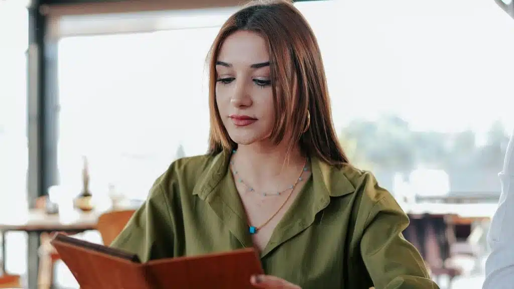 A woman in a green shirt looks down while reading a menu.