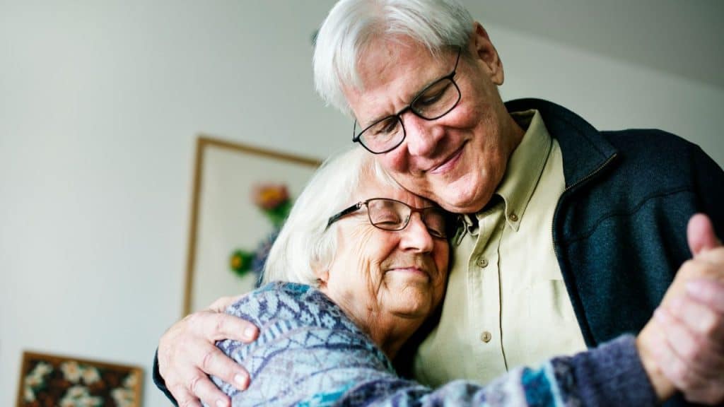 Close-up of an elderly couple affectionately hugging, smiling with their eyes closed.