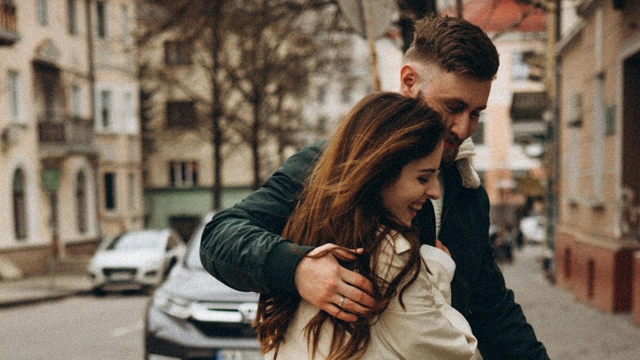 A man and woman kissing while walking on a sidewalk.