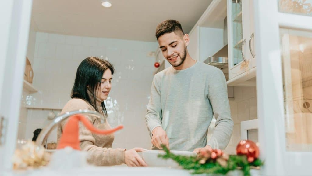 Man cutting something in a white bowl while a woman watches in a kitchen.