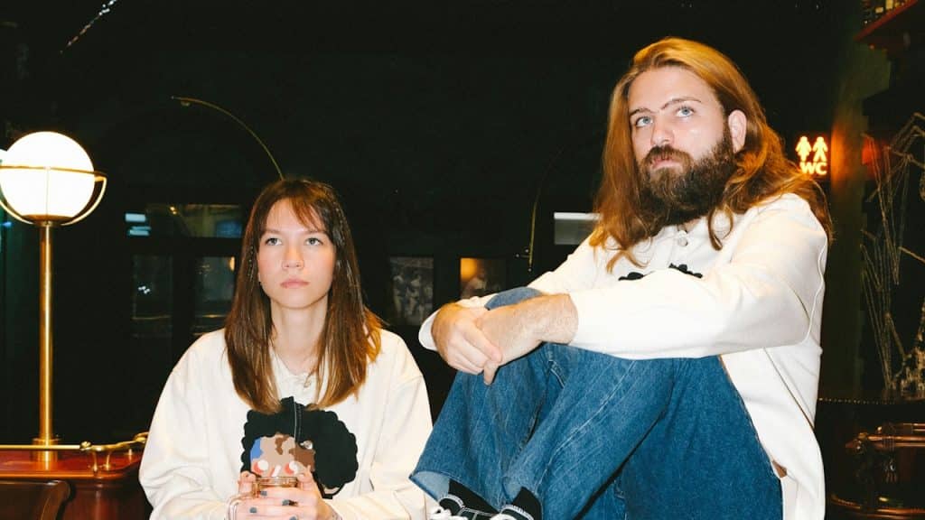 A woman in a long-sleeve white shirt is sitting beside a man in blue denim jeans.