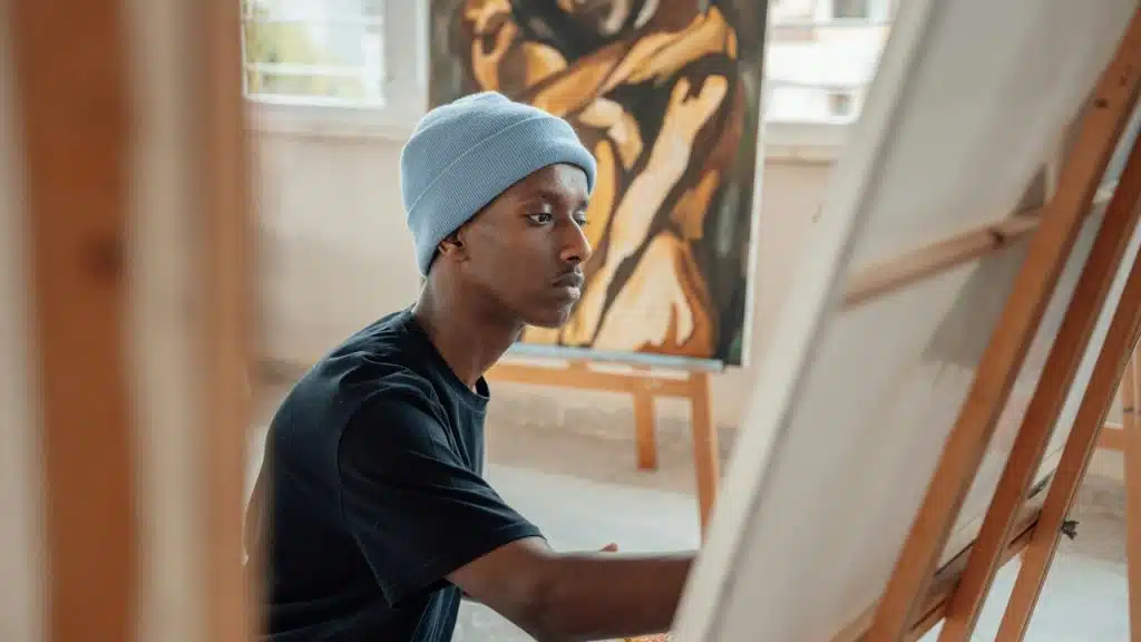 A man in a beanie painting on a canvas.