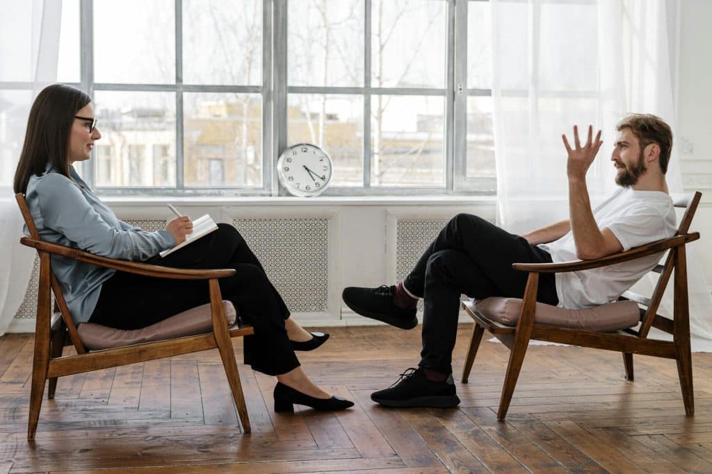 A man sitting on a wooden chair during a therapy session.