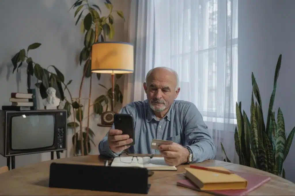 An older man holding his cellphone and a credit card.