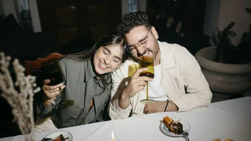 Smiling couple happily cheers with wine glasses at a table with dessert plates.